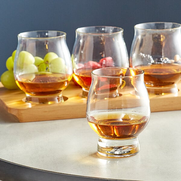 A table with glasses of bourbon and fruit on it, including a Reserve by Libbey Kentucky Bourbon Trail Tasting Glass filled with bourbon and grapes.