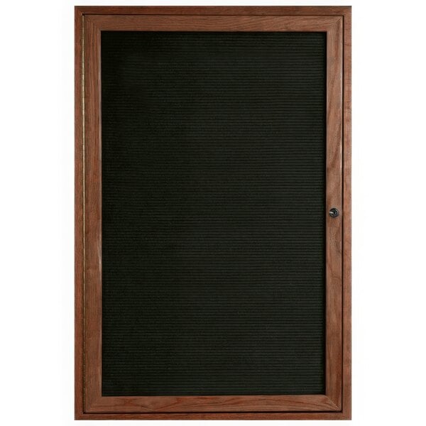 An Aarco black felt message board with a walnut frame on a black wooden door.