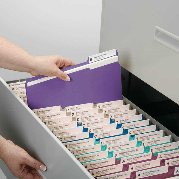 A hand putting a purple Smead file folder into a file drawer.