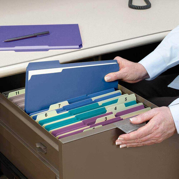 A person putting Smead assorted color file folders in a file drawer.