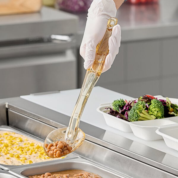 A hand using a Cambro amber perforated spoon to serve food from a white container.