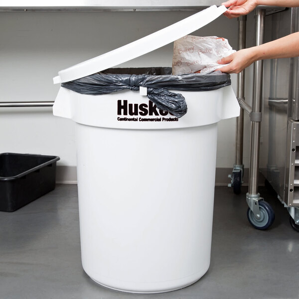 A woman putting a plastic bag into a white Continental Huskee trash can.