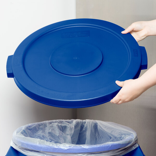 A person holding a blue lid over a Carlisle Bronco trash can.