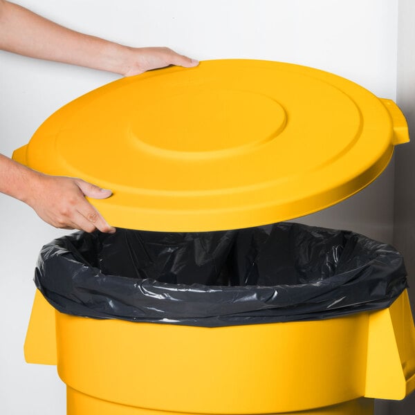 A hand placing a yellow Carlisle Bronco trash can lid on a yellow trash can.