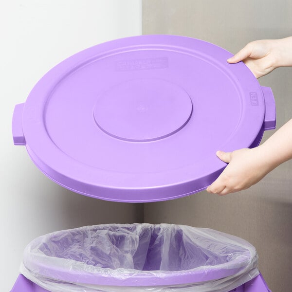 A person placing a purple Carlisle Bronco lid on a purple trash can