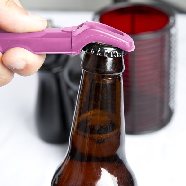 A hand using a Franmara pink plastic bottle opener to open a brown bottle.