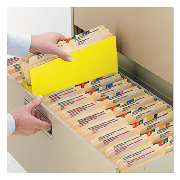 A hand holding a Smead yellow letter size file folder in a drawer with other file folders.