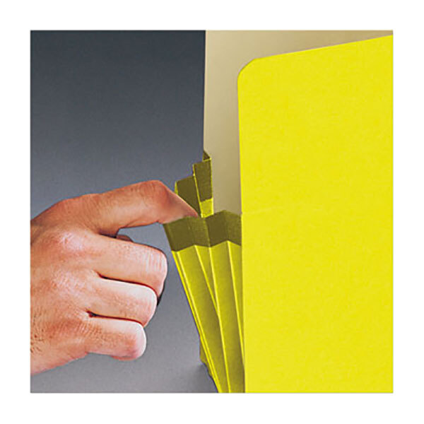 A hand opening a yellow Smead legal size file pocket with a black border on the tab.