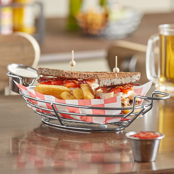 A sandwich in an American Metalcraft oblong wire basket with fries and sauce.