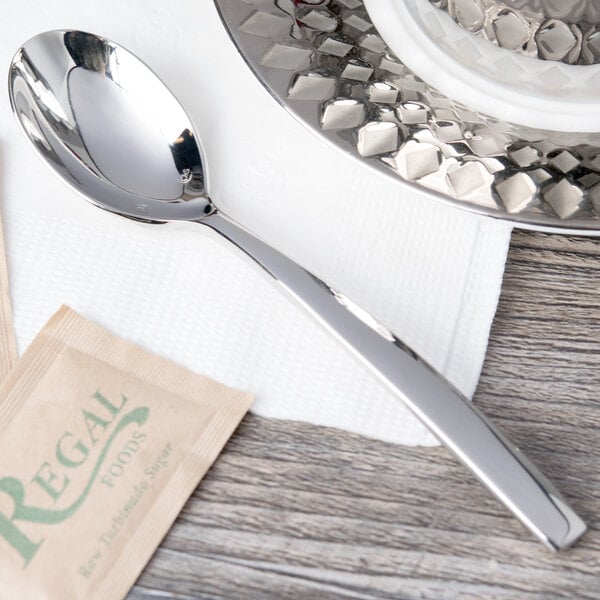 A Chef & Sommelier stainless steel teaspoon on a saucer on a table.