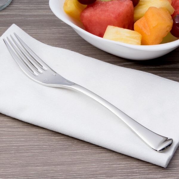 A Chef & Sommelier stainless steel dessert fork on a napkin next to a bowl of fruit.