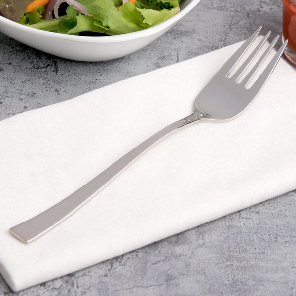 An Arcoroc stainless steel salad fork on a napkin next to a bowl of salad.