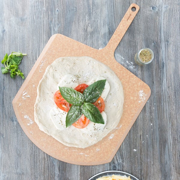 A pizza with tomatoes and basil on a Epicurean wood pizza peel.