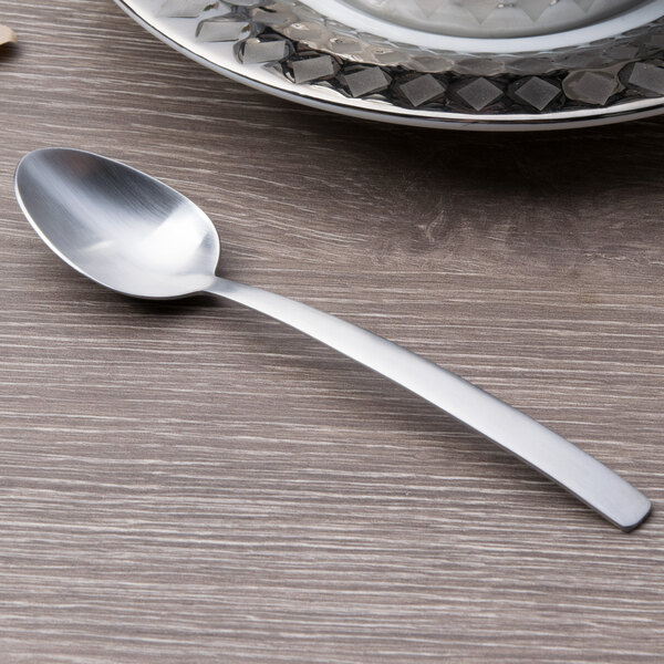 An Arcoroc stainless steel demitasse spoon with a silver handle on a table.