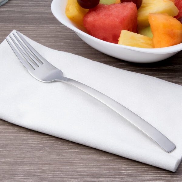 An Arcoroc stainless steel dessert fork on a napkin next to a bowl of fruit.