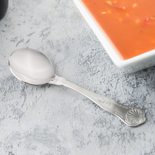 A Libbey stainless steel bouillon spoon next to a bowl of soup.