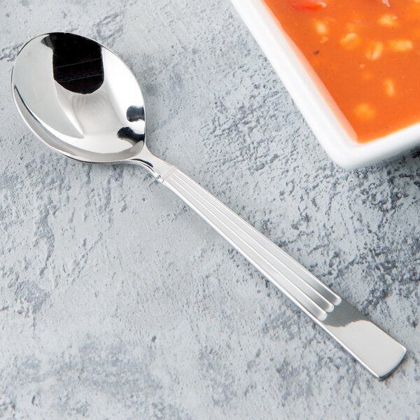 A Libbey stainless steel bouillon spoon next to a bowl of soup.