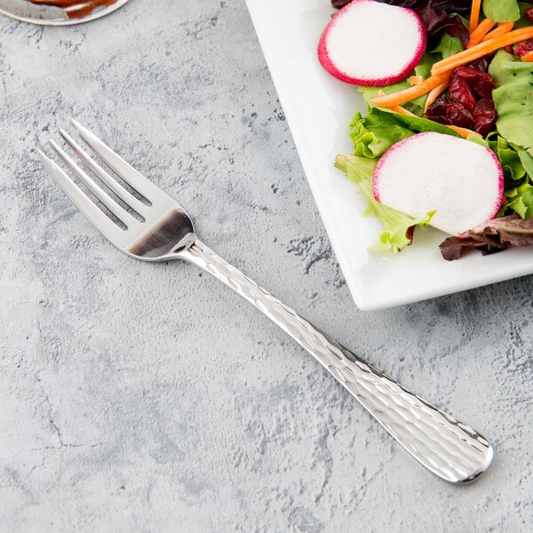 A Libbey stainless steel salad fork next to a plate of salad.