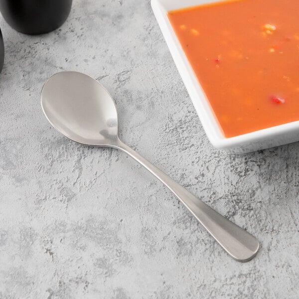 A Libbey stainless steel bouillon spoon next to a bowl of soup.