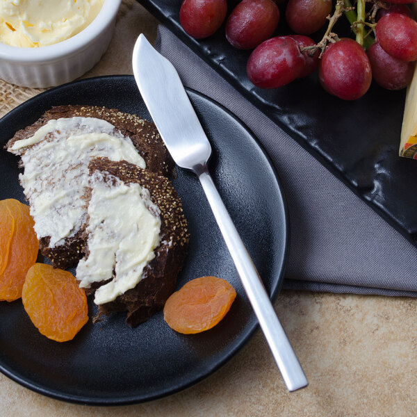 A Libbey stainless steel butter spreader on a plate with bread and fruit.