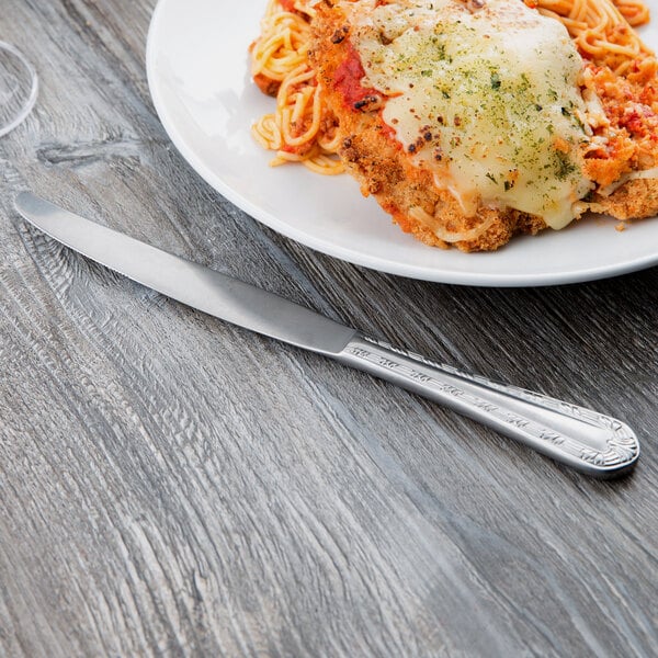 A Libbey stainless steel dinner knife next to a plate of spaghetti with meat and cheese.