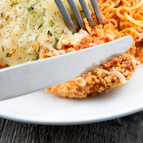 A knife cutting food on a plate with a fork.