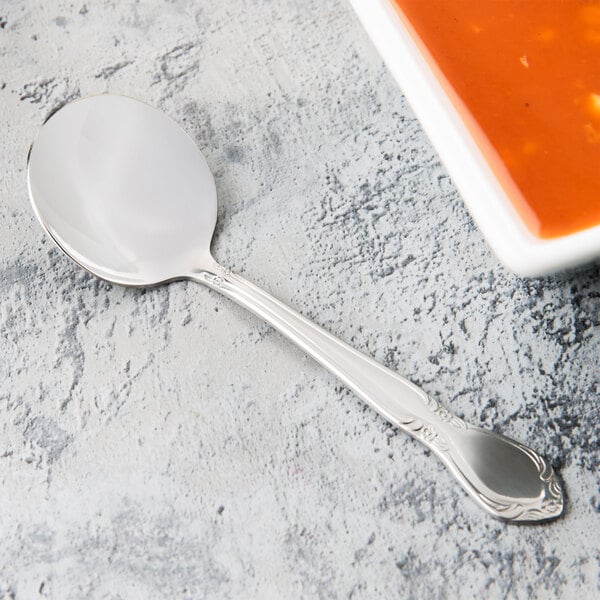 A Libbey Lady Astor stainless steel bouillon spoon next to a bowl of soup.