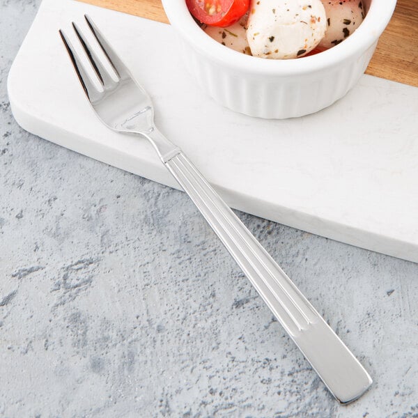 A Libbey stainless steel cocktail fork next to a white bowl of food.