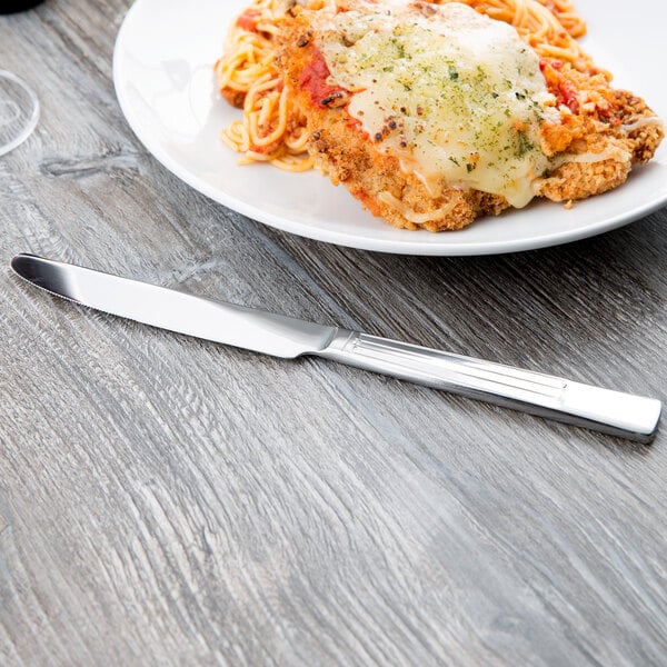 A Libbey stainless steel dinner knife next to a plate of food on a table.