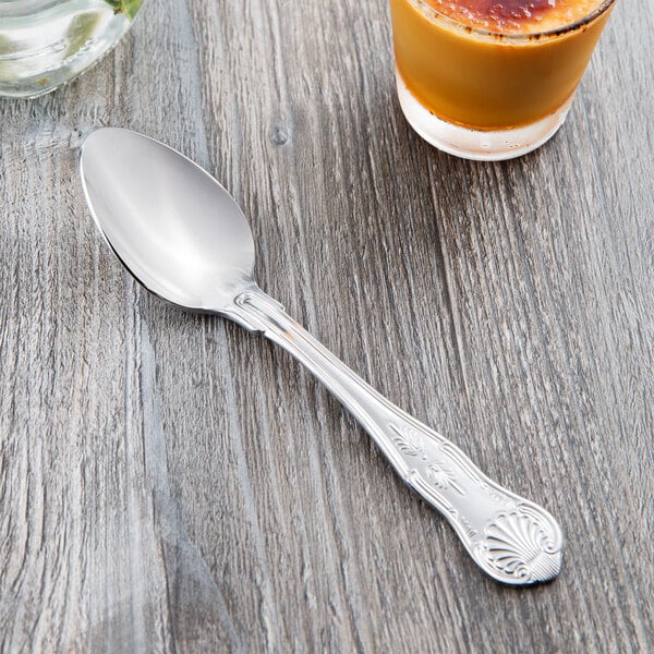 A Libbey stainless steel dessert spoon on a table next to a glass of juice.