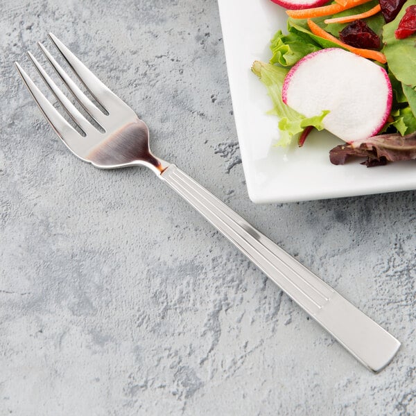 A Libbey stainless steel salad fork next to a plate of salad.