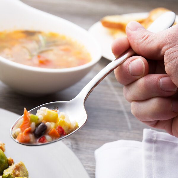 A person holding a Chef & Sommelier stainless steel dinner spoon filled with food over a plate.