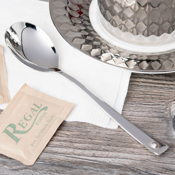 An Arcoroc stainless steel teaspoon on a saucer with a tea bag.