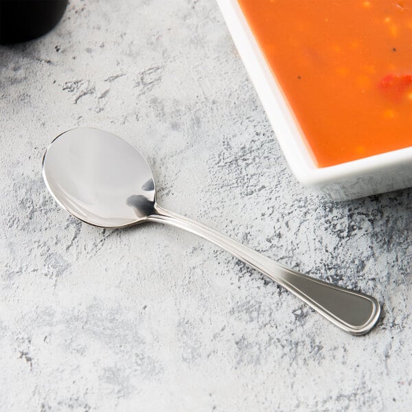 A Libbey stainless steel bouillon spoon next to a bowl of soup.