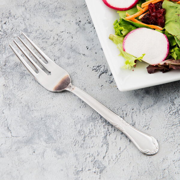 A Libbey stainless steel salad fork next to a plate of salad.