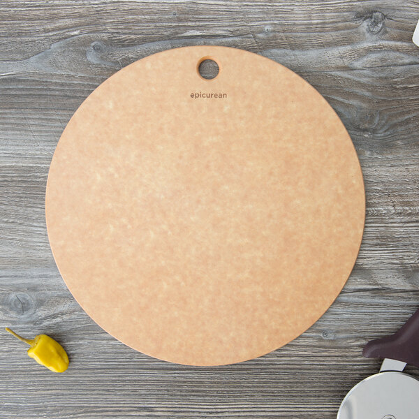 A round Epicurean natural wood fiber pizza board with a pizza cutter and pepper on a table.