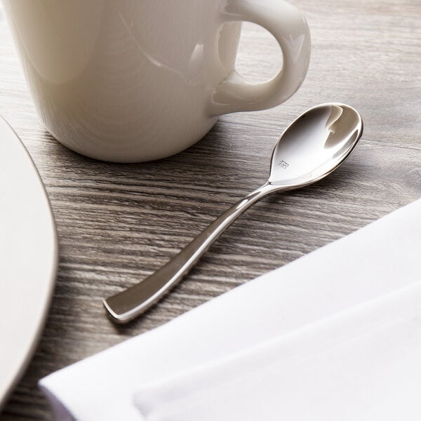 A Chef & Sommelier stainless steel demitasse spoon on a table next to a white mug.