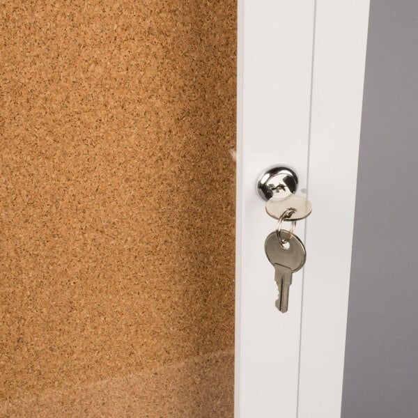 The key is in the door lock of a white Aarco bulletin board cabinet.