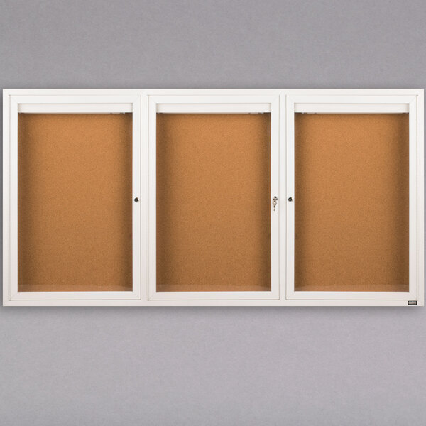 A white Aarco indoor bulletin board cabinet with 3 cork boards behind glass doors.