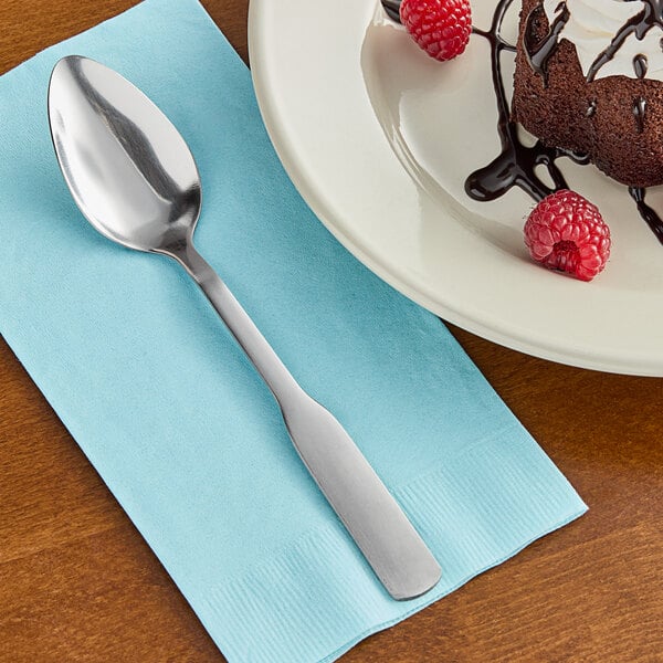 A Choice stainless steel medium weight dinner/dessert spoon on a napkin next to a chocolate cake.