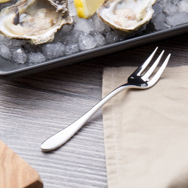 A Chef & Sommelier stainless steel oyster fork on a plate of oysters.