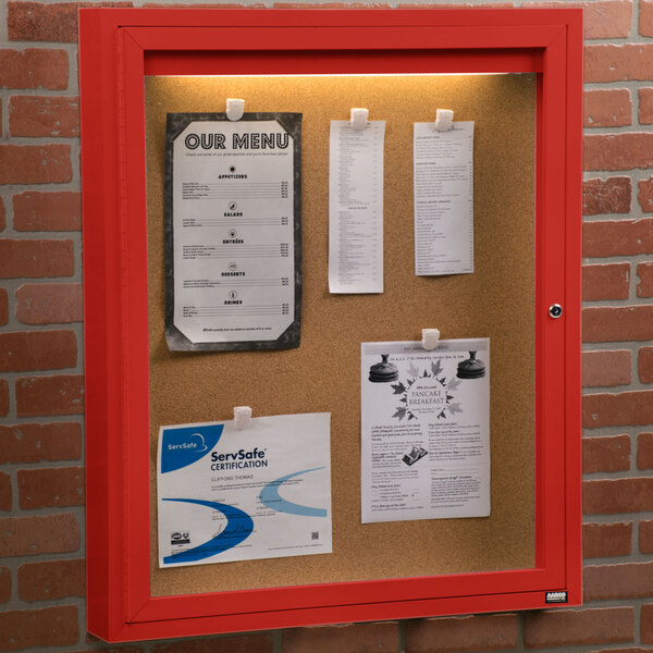 An Aarco red powder coated indoor bulletin board cabinet with 1 door.