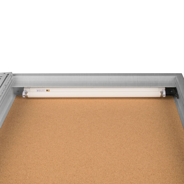 An Aarco satin anodized metal bulletin board cabinet with a light inside.