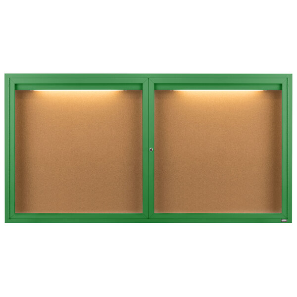 A green framed bulletin board with 2 doors and lights on the wall.