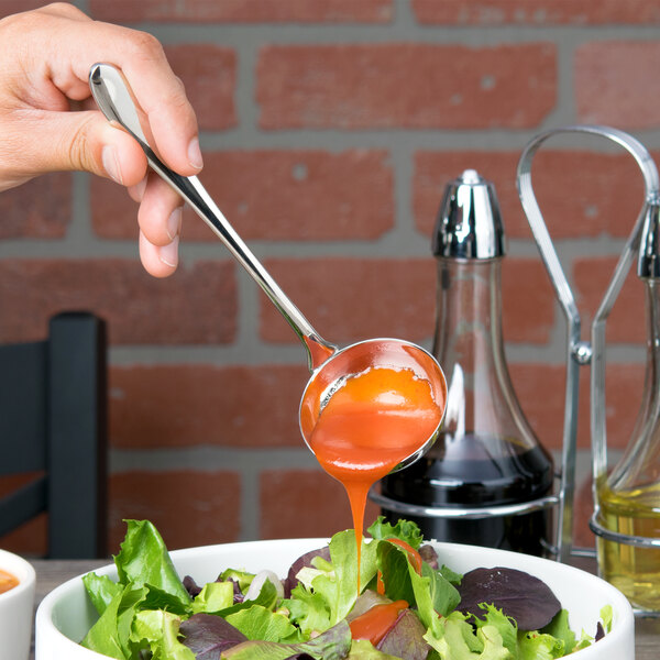 A hand using a Chef & Sommelier stainless steel sauce ladle to pour sauce onto a salad.