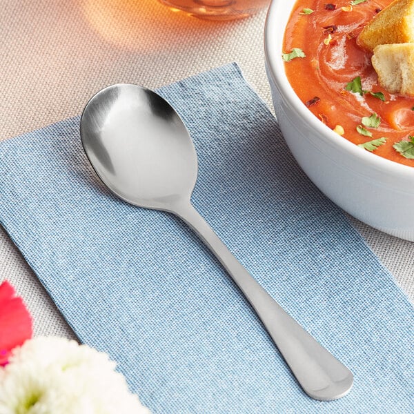 A bowl of soup with a Choice medium weight stainless steel bouillon spoon on a napkin.