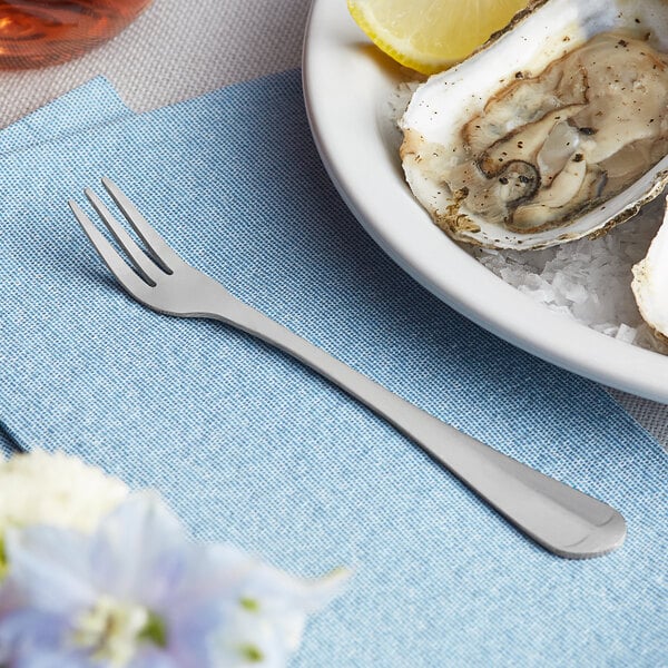 A Choice Medium Weight stainless steel oyster fork next to a plate of oysters and lemon slices.