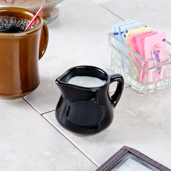 A black Tuxton china creamer with a lid on a counter.