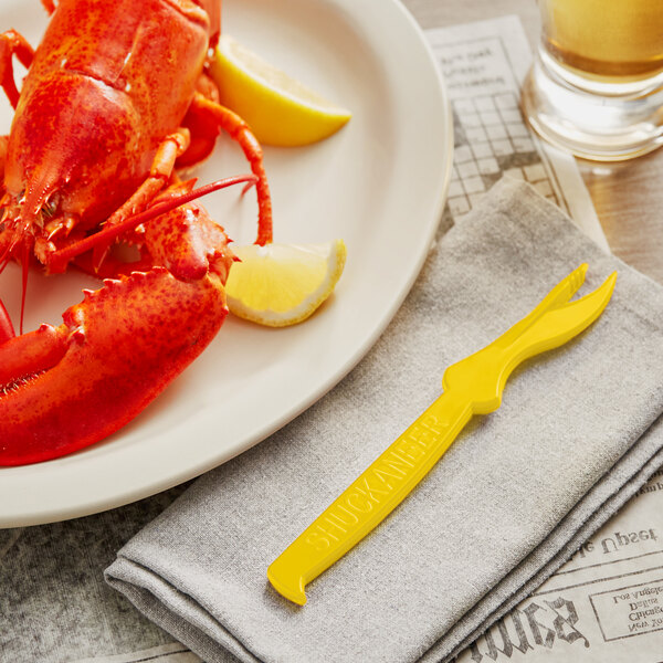 A lobster on a plate with a yellow Choice Shuckaneer seafood sheller and lemon slices.