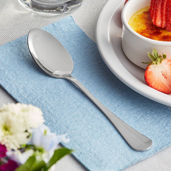 A Choice medium weight stainless steel spoon on a plate with a bowl of creme brulee and strawberries.